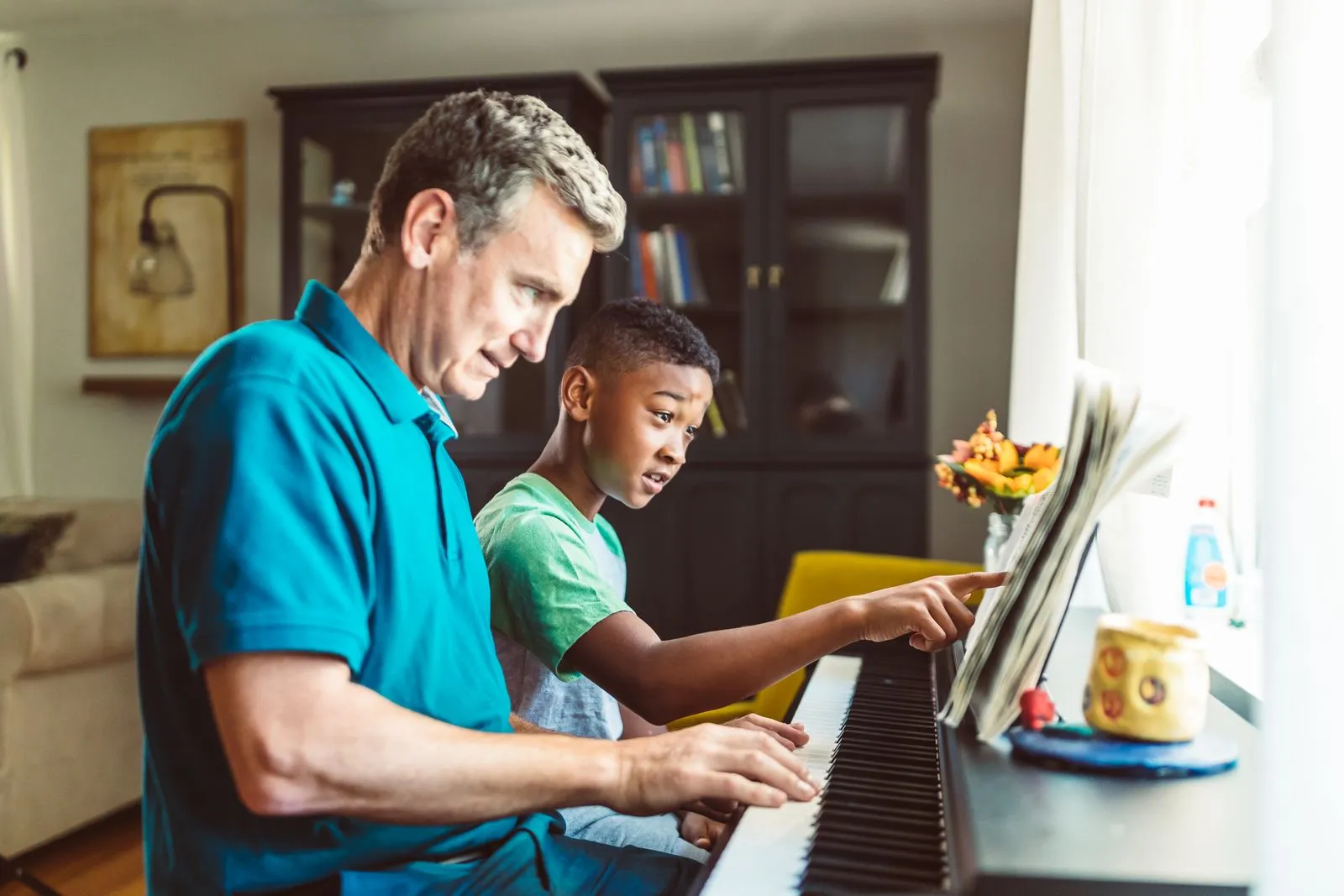 Father teaching son to play the piano, sharing a musical moment together indoors.